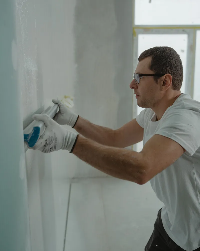 A worker sanding a finished drywall wall by hand.