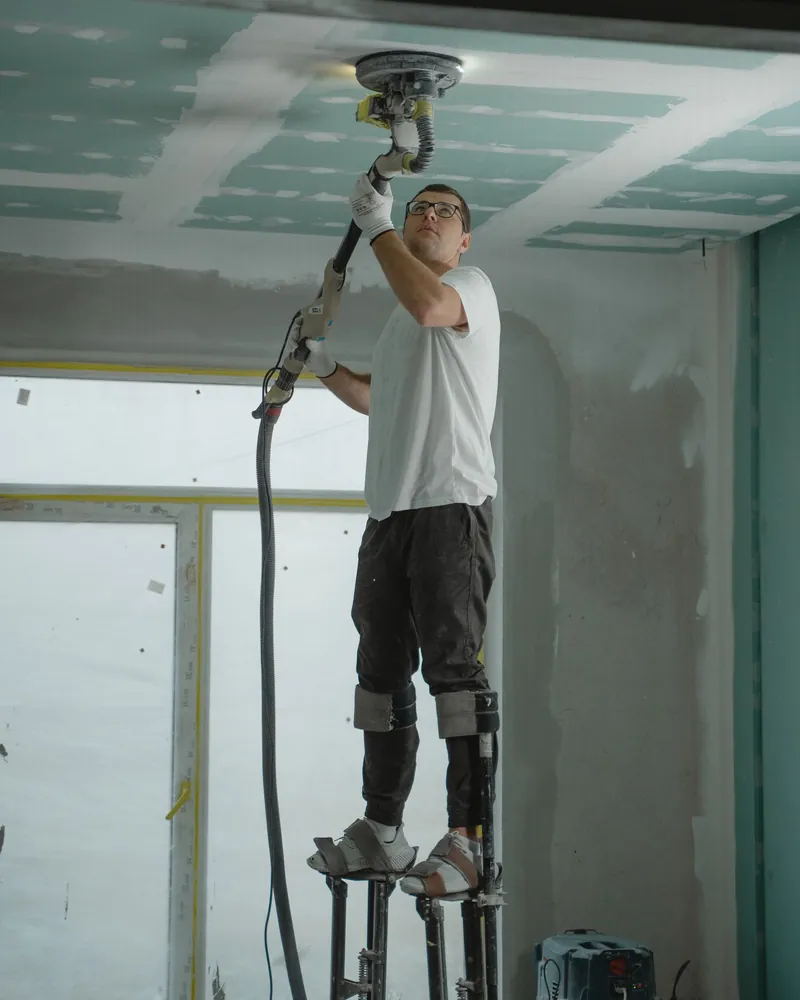 A finisher on stilts spraying texture onto a ceiling.